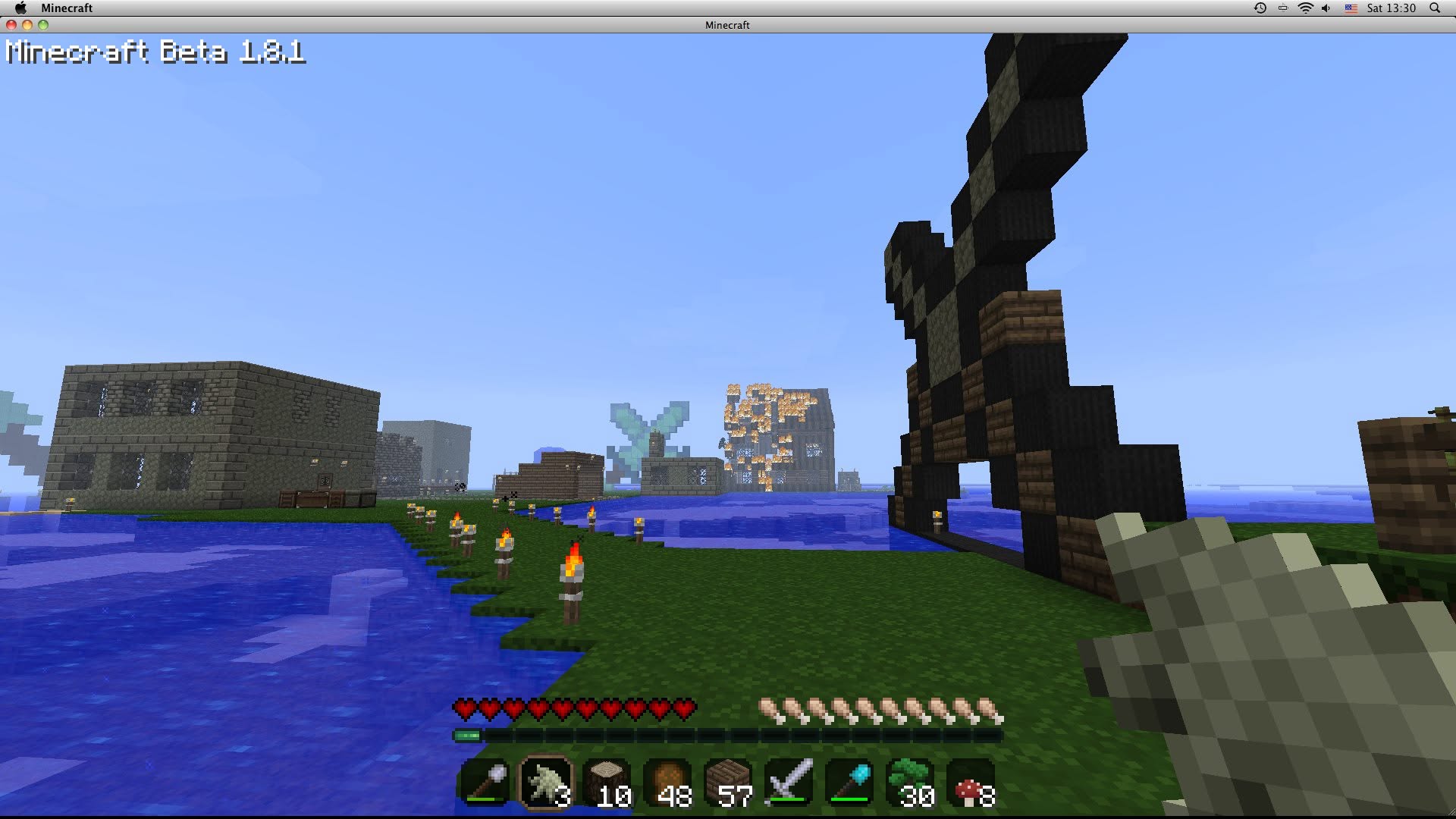 A Minecraft Beta 1.8.1 screenshot showing early player builds along a lake, lit by torches